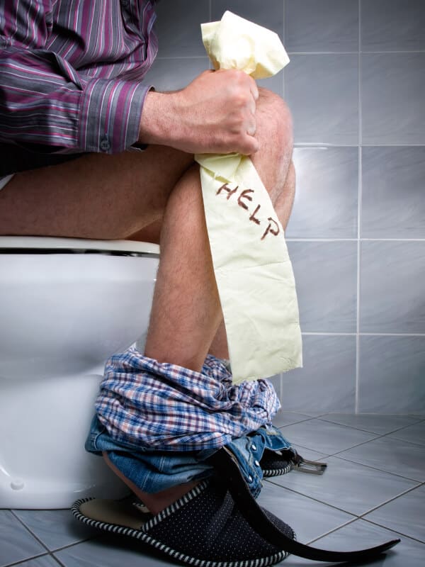 مردی که روی توالت فرنگی نشسته و روی دستمالی که به دست دارد به منظور درمان اسهال کلمه کمک نوشته شده است