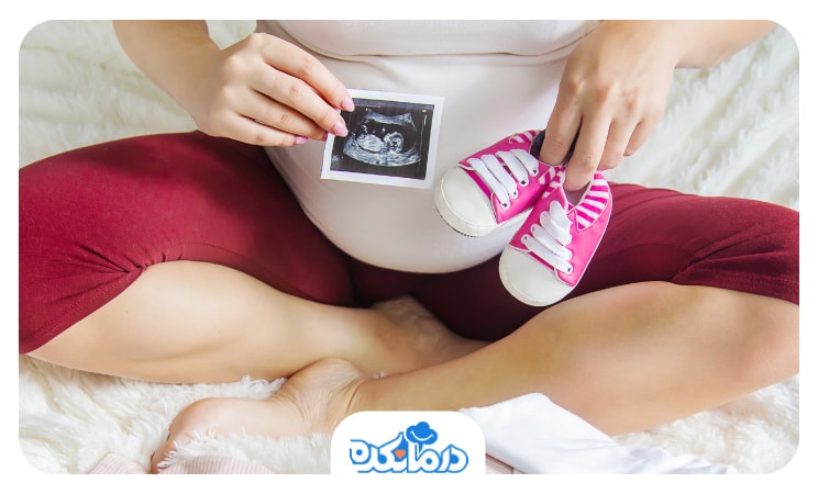 تصویر یک زن باردار با یک کفش دخترانه و عکس سونوگرافی رو شکمش قرار داده
