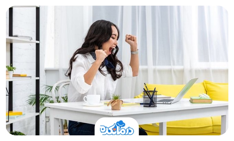 تصویر زنی که پست لپ تاپ و میز خود نشسته و از شدت خوشحالی و شعف، جیغ میزند و دستانش را به سمت بالا مشت کرده