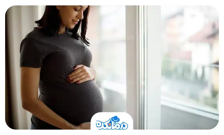 زن بارداری که کنار پنجره ایستاده است