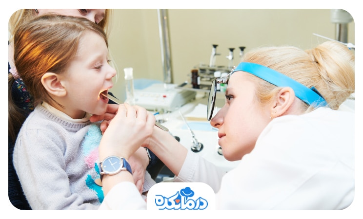 تصویر کودکی که در مقابل دکتر گوش و حلق و بینی قرار گرفته و دکتر در حال معاینۀ دهان کودک است.