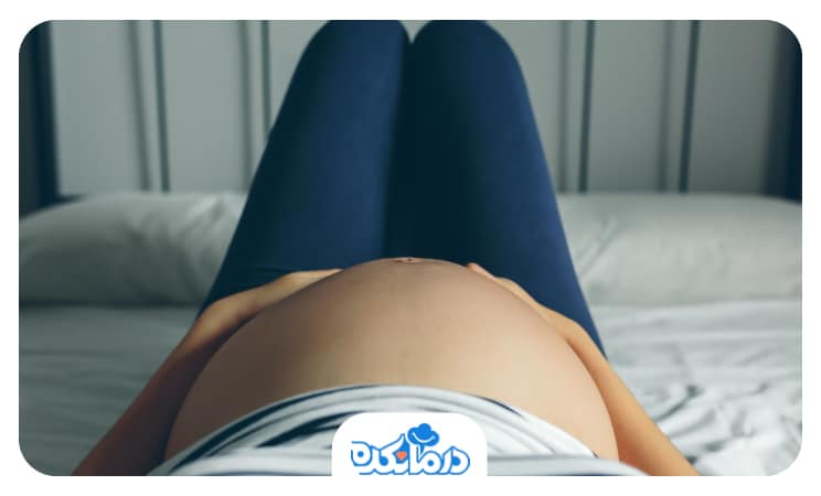 تصویر خانم بارداری که دراز کشیده و شکم خود را میمالد.