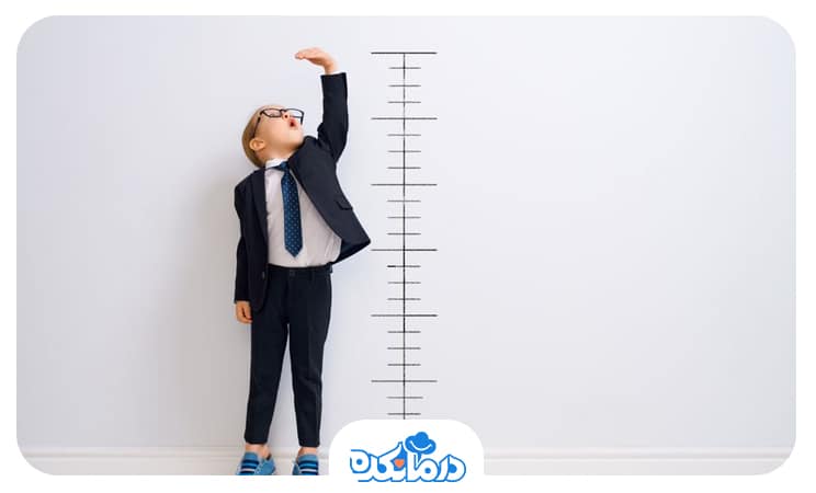 پسر بچه‌ای که در کنار دیوار ایستاده و از روی خطوط رسم شده روی آن قد خود را اندازه می‌گیرد