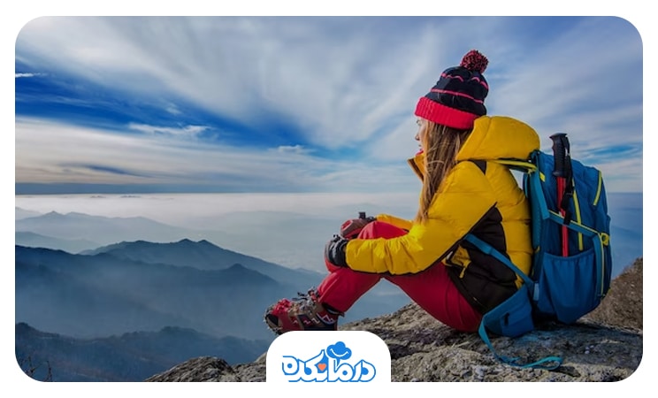 زن کوهنوردی که روی کوه نشسته و به اطراف نگاه می‌کند
