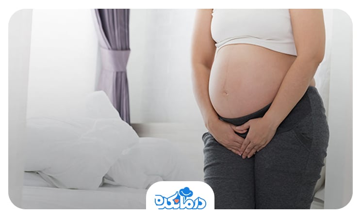زن بارداری که روبروی تخت ایستاده و  به دلیل تجربه علائم بارداری 2 دست خود را جلوی بدن گذاشته است