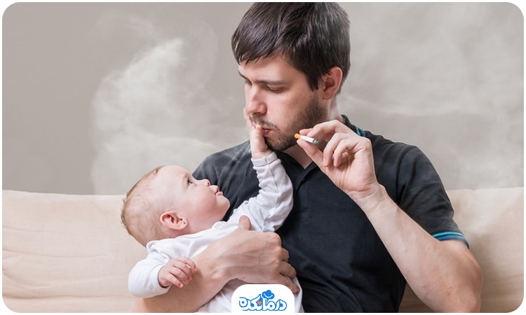 یک مرد در حالی که نوزاد را بغل کرده است سیگار می‌کشد