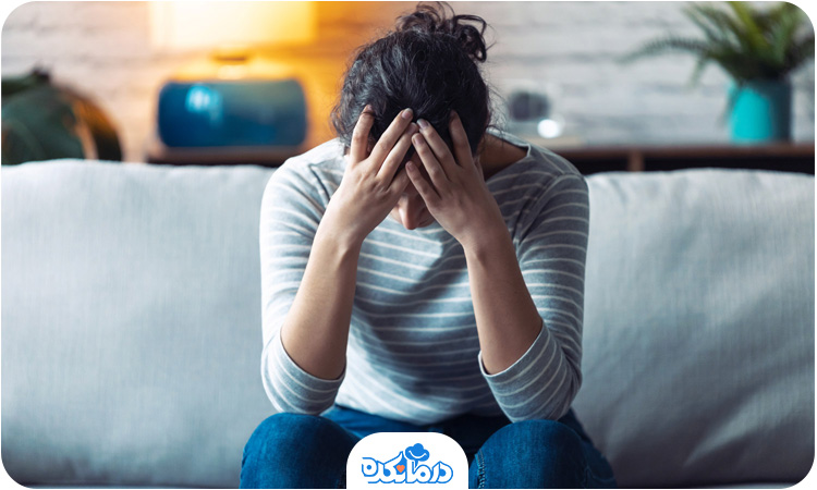 یک زن جوان افسرده که روی مبل نشسته و با دستهایش سر خود را گرفته است