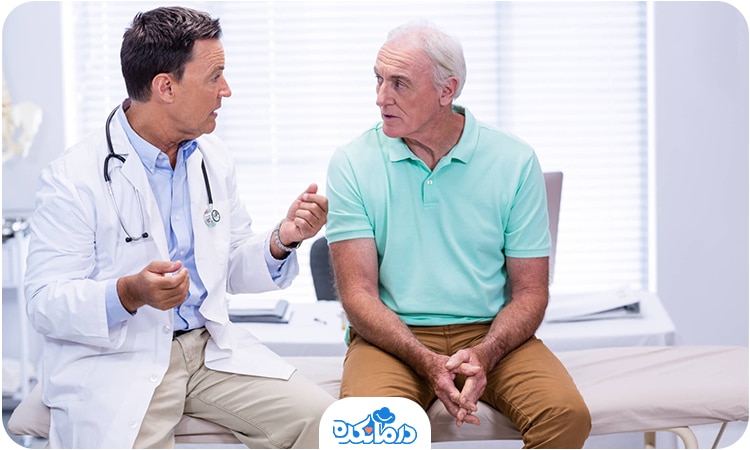 یک مرد سالمند و یک پزشک که روی تخت معاینه نشسته‌اند و با هم صحبت می‌کنند