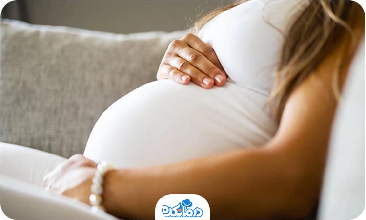یک زن باردار که نشسته و دست خود را روی شکم قرار داده است