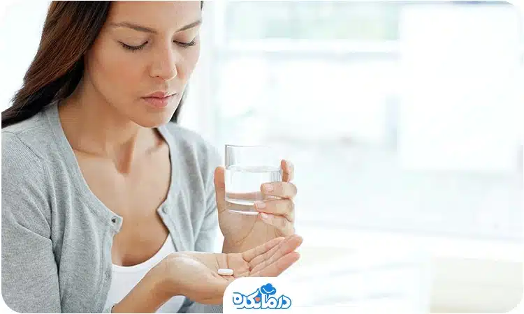 تصویر خانمی در حال خوردن قرص همراه با یک لیوان آب