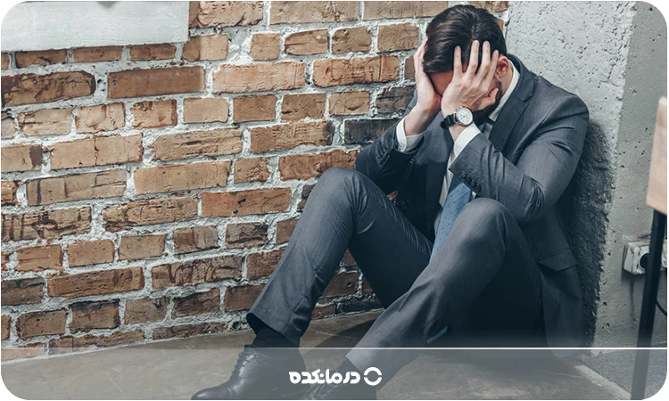 تصویر فردی که با ناراحتی گوشه‌ای نشسته را می‌بینید