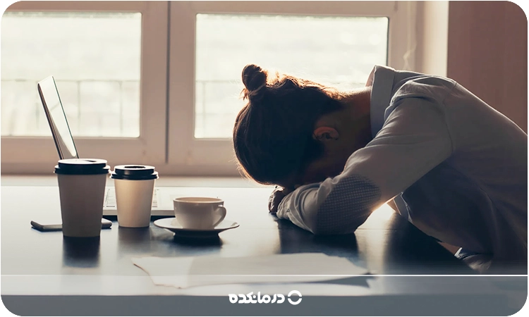 تصویر یک خانم که سرش را روی میز کار گذاشته را می‌بینید