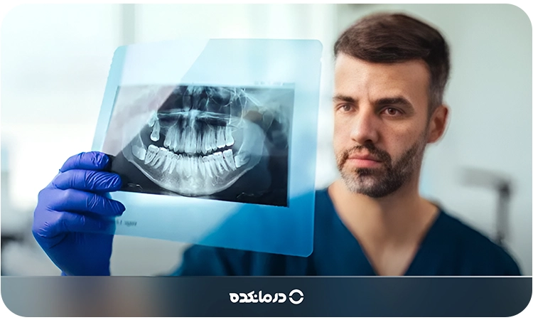 تصویر دندانپزشک در حال بررسی عکس رادیولوژی را می‌بینید