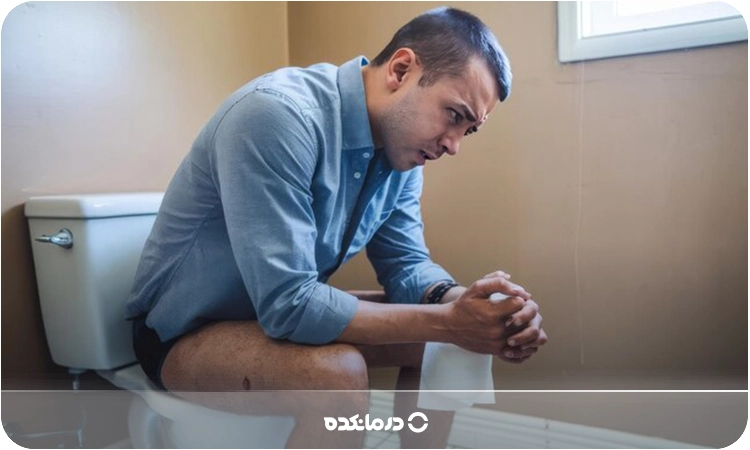 تصویر مردی که با ناراحتی و احساس درد روی توالت فرنگی نشسته را میبینید