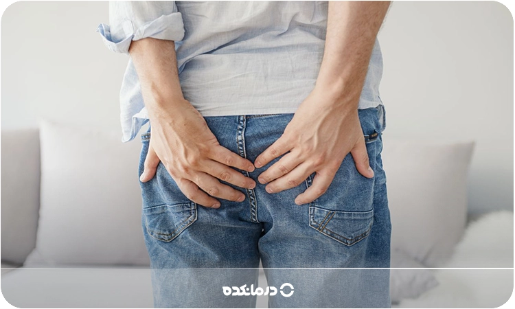 تصویر یک آقا که به دلیل درد دستش روی ناحیه مقعدش است را میبینید