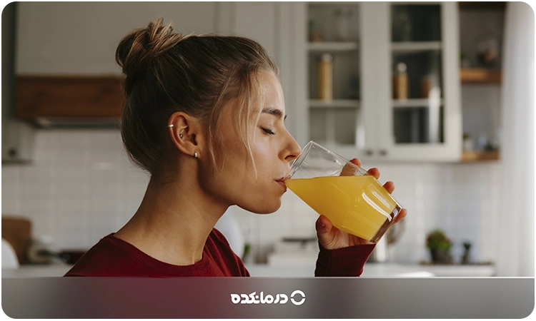 تصویر خانمی در حال نوشیدن یک لیوان آب پرتقال میبینید
