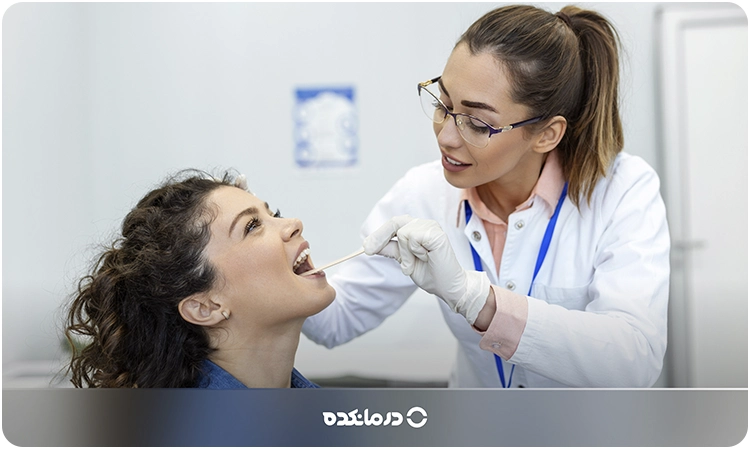 تصویر پزشکی که در حال معاینه دهان بیمار است.
