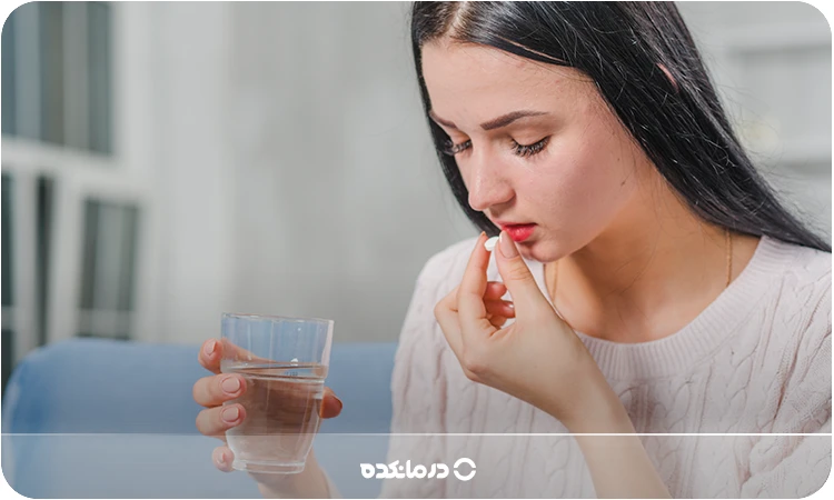 تصویر خانمی در حال خوردن قرص همراه با یک لیوان آب را می بینید