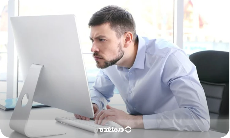 تصویر فرد پشت لپ‌تاپ را می بینید که شانه‌های او جلو آمده و سر خم‌شده

