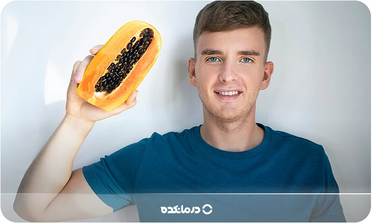 تصویر مردی که در حال خوردن میوه پاپا است را می بینید