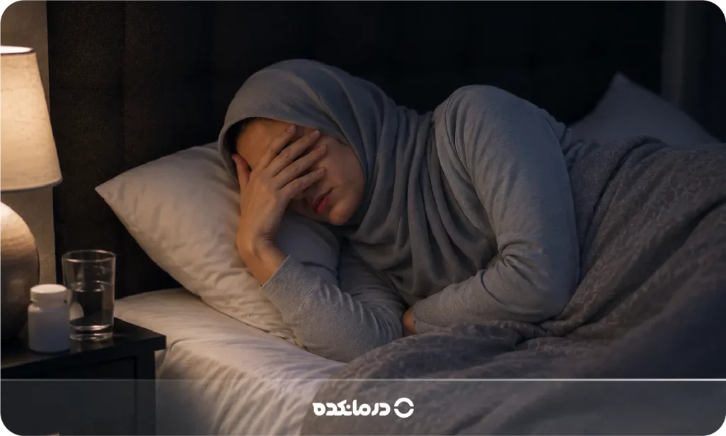 تصویر فردی که درون تختخواب است و به دلیل درد، دستش را روی پیشانی خود گذاشته را می بینید