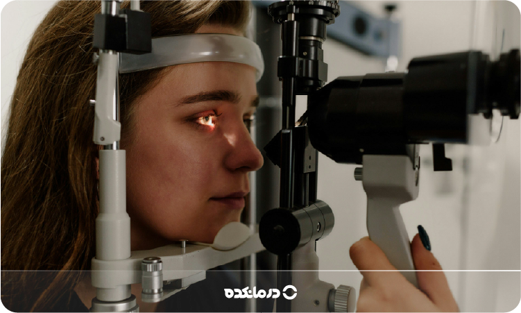 تصویر فردی که ‌پزشک در حال معاینه چشم‌های او با دستگاه است را می بینید