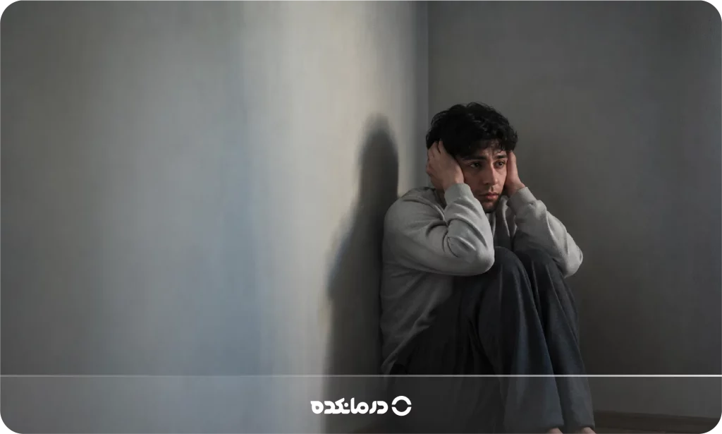 تصویر فرد ناراحت یا بهتزده که در گوشهای نشسته را می بینید