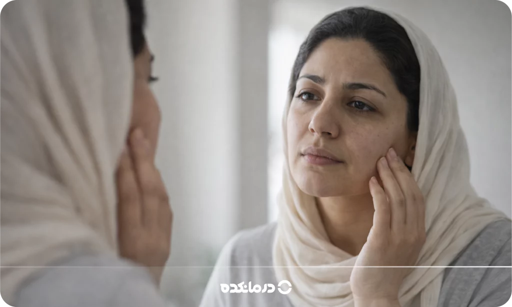تصویر زنی که در آینه به پوست صورت خود نگاه می‌کند را می بینید