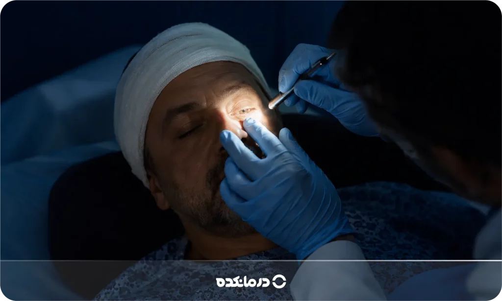 تصویر پزشک در حال معاینه چشمهای بیمار که روی تخت دراز کشیده و بیهوش است